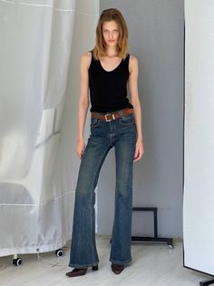 Woman in a black tank top and flared jeans posing in a studio