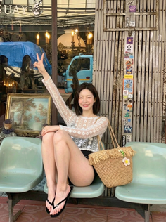 Woman in a lace top and black shorts sitting outdoors with a straw bag