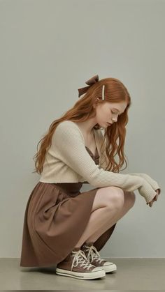 Woman with long red hair in a brown dress and cardigan, squatting indoors