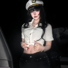 Woman in a captain hat and tied white shirt exposing her midriff at night