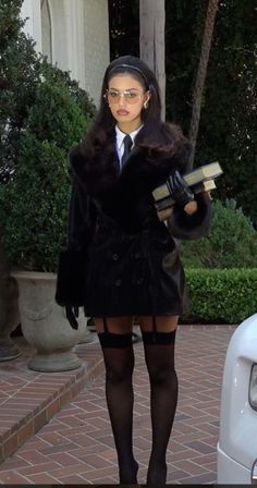 Woman in a black coat, stockings, and garter belt holding books outdoors