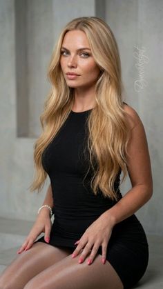 Woman with long blonde hair wearing a black dress and pearl bracelet indoors