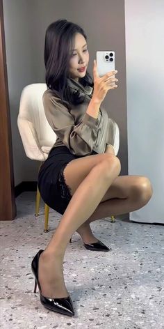 Woman in a satin blouse and black skirt taking a mirror selfie