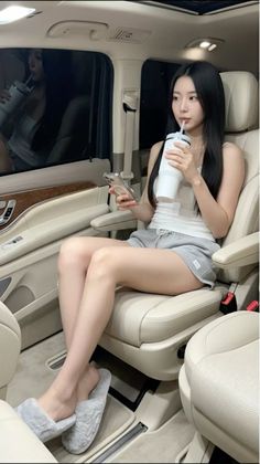 Woman in a tank top and shorts sitting in a car interior, drinking from a cup