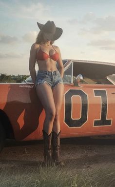 Woman in a cowboy hat, red bikini top, and denim shorts leaning on an orange car