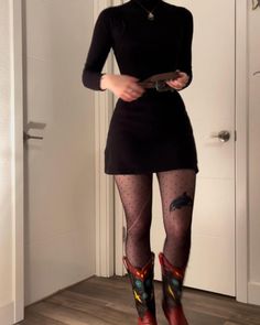 Person in a black dress, polka dot tights, and cowboy boots indoors