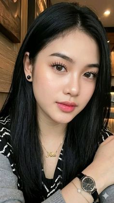 Woman with long black hair wearing a gold necklace and black watch
