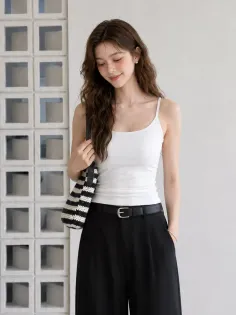 Woman with long wavy hair wearing a white camisole and black pants indoors