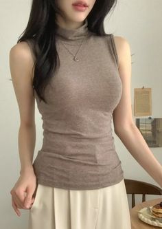 Woman in a sleeveless turtleneck top and light pants indoors