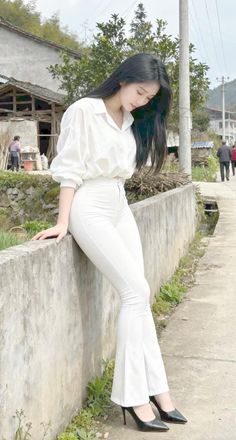 Woman in a white shirt and pants leaning on a wall outdoors