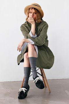 Person in a straw hat and green jacket sitting on a chair indoors