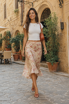 Woman in a floral skirt and white top walking on a cobblestone street