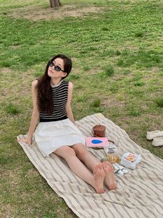 Woman with long hair and sunglasses sitting on a picnic blanket in the grass