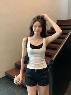 Woman in a white tank top and black shorts holding a drink indoors