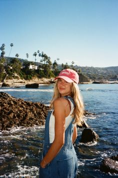 Young woman in denim overalls and a pink cap at a rocky beach with palm trees