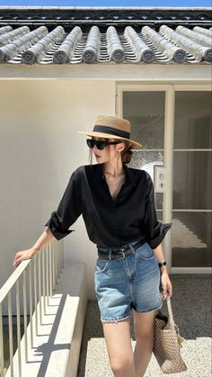 Woman in a straw hat and sunglasses wearing a black shirt and denim shorts outdoors