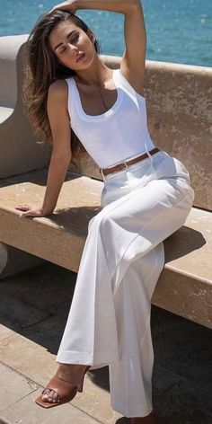 Woman in a white tank top and white pants sitting outdoors