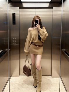Woman in a knitted dress and knee-high boots taking a mirror selfie in an elevator