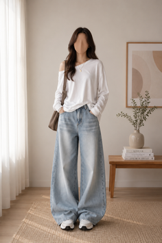 Woman in a white long-sleeve shirt and wide-leg jeans standing indoors
