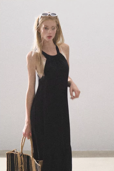 Woman in a black halter dress with sunglasses on her head, holding a straw bag