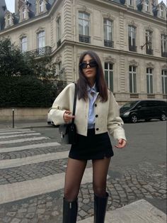 Woman in a cropped jacket, mini skirt, and knee-high boots on a city street