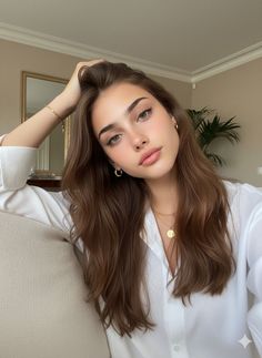 Woman with long brown hair wearing a white shirt and gold jewelry indoors