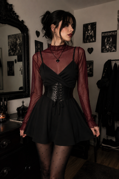 Woman in a black dress with a corset and sheer top in a gothic-themed room