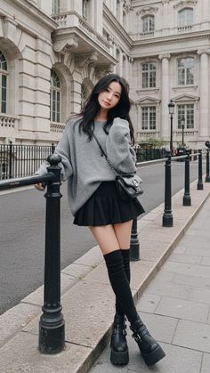 Woman in a grey sweater and black pleated skirt with thigh-high boots on a street