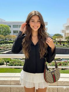 Smiling woman with long wavy hair in a black shirt and white skirt outdoors