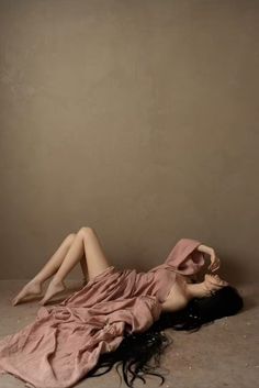 Woman with long black hair draped in pink fabric, lying on a warm-toned floor