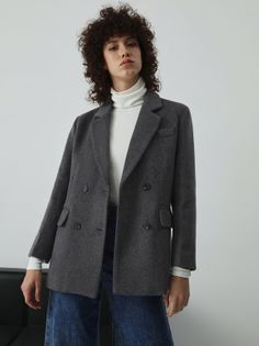 Woman with curly hair wearing a gray blazer and white turtleneck