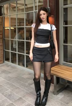 Woman with long hair wearing a crop top, mini skirt, and black boots outdoors