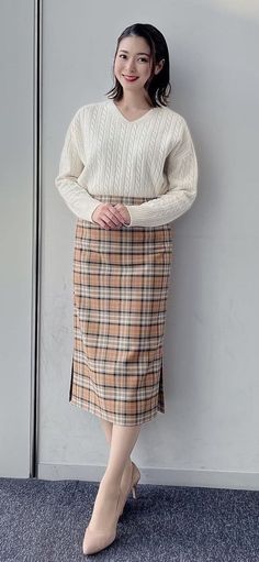 Woman in a white cable knit sweater and plaid skirt posing indoors
