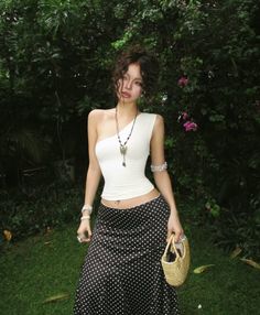 Woman with curly hair wearing a one-shoulder top and polka dot skirt outdoors