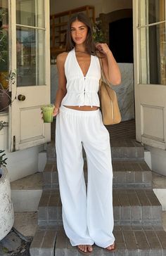 Woman in a white halter top and wide leg pants holding a green drink