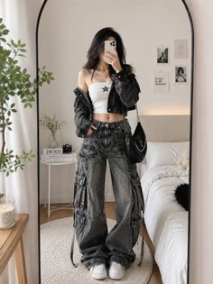 Person in a crop top, denim jacket, and cargo pants taking a mirror selfie in a bedroom
