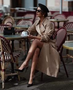 Woman in a trench coat and beret sitting at an outdoor cafe