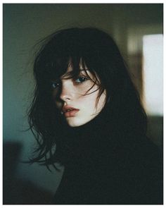 Woman with dark hair and a black turtleneck in soft indoor lighting
