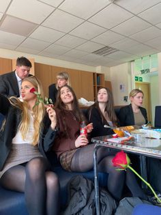Multiple young adults sitting indoors, some holding red roses