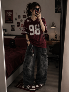 Person in an oversized jersey and baggy cargo pants taking a mirror selfie indoors