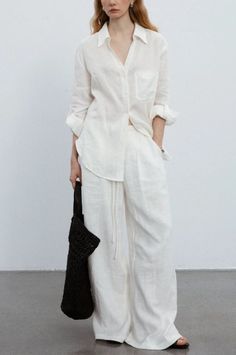 Woman in a white linen shirt and wide leg pants holding a black bag