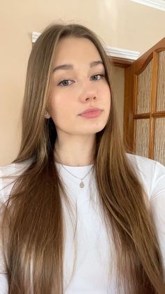 Young woman with long brown hair wearing a white shirt and necklace indoors