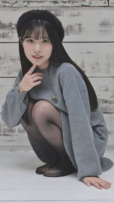 Woman with long black hair and a beret, squatting indoors