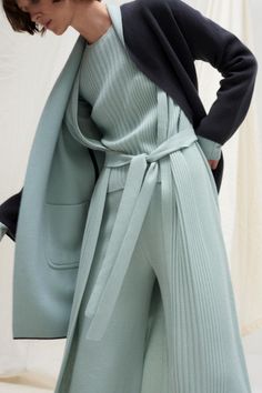 Woman in a mint green ribbed outfit with a dark blue cardigan and belted waist