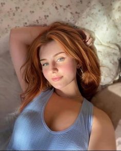 Woman with red hair and blue eyes wearing a light blue top, lying down