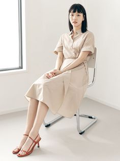 Woman in a beige dress and red sandals sitting on a chair indoors