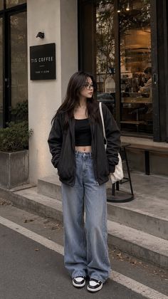 Woman in a black crop top and loose jeans standing outside a coffee shop
