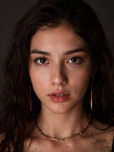 Woman with long dark hair and gold jewelry against a dark background