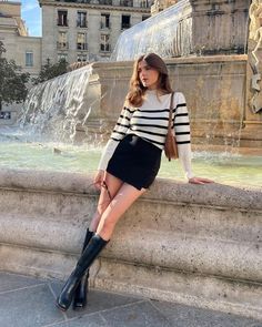 Woman in a striped sweater and mini skirt posing by a fountain