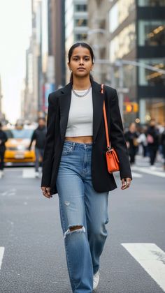 Woman in a black blazer and ripped jeans walking on a city street